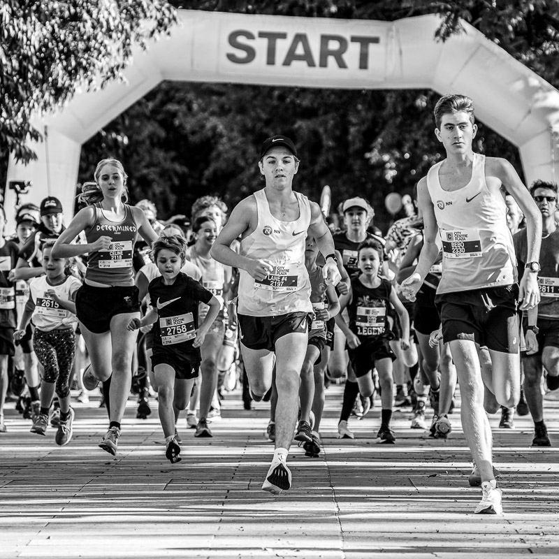 Low angle of people running toward the camera, with start line of charity fun run in background